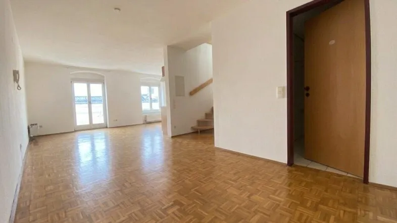 Geräumiges Wohnzimmer mit Fischgrätparkett, hellen Wänden und Zugang zu einem Balkon.