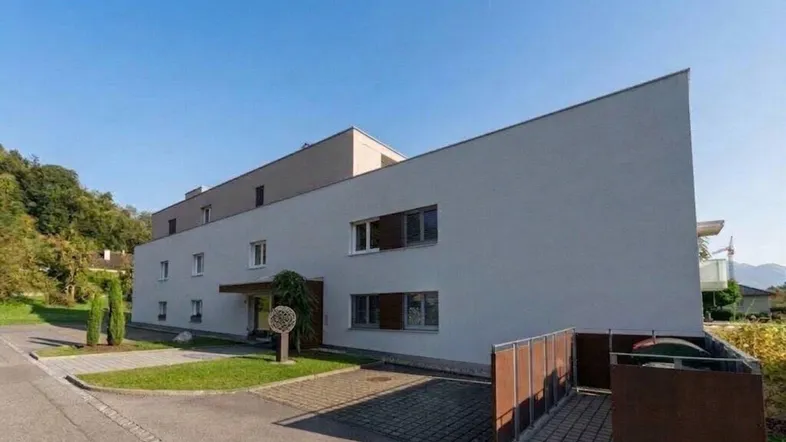 Modernes Mehrfamilienhaus mit klarer Architektur und gepflegter Außenanlage unter blauem Himmel.
