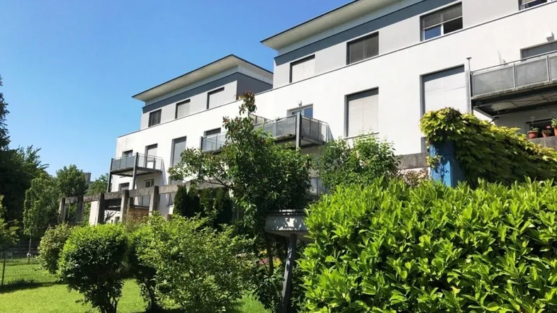 Mehrere moderne Wohngebäude mit Balkonen und gepflegter Grünanlage unter blauem Himmel.