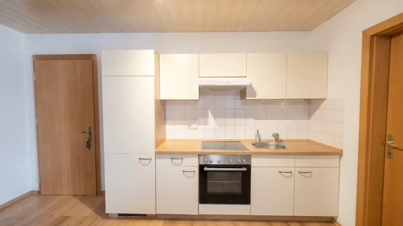 Kleine Einbauküche mit hellen Schränken, Holzarbeitsplatte und Laminatboden in einem hellen Raum.