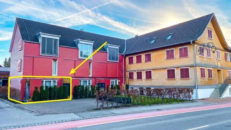 Außenansicht eines Gebäudes mit roter und holzverkleideter Fassade unter blauem Himmel.