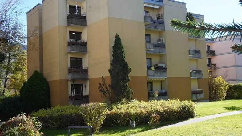 Mehrstöckiges Apartmentgebäude mit mehreren Balkonen und gepflegter Grünanlage im Freien.