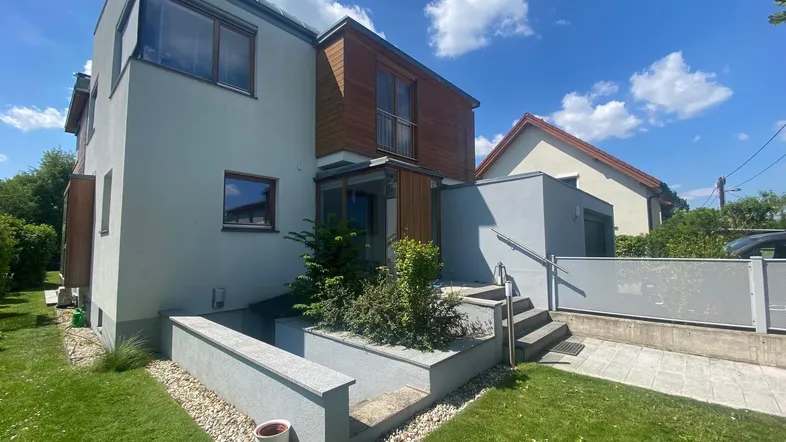 Modernes Haus mit heller Fassade, Holzverkleidung und Zugang zum Gartenbereich.