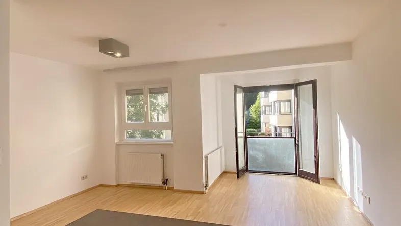 Helles Wohnzimmer mit Parkettboden, weißen Wänden und Zugang zu einem Balkon.