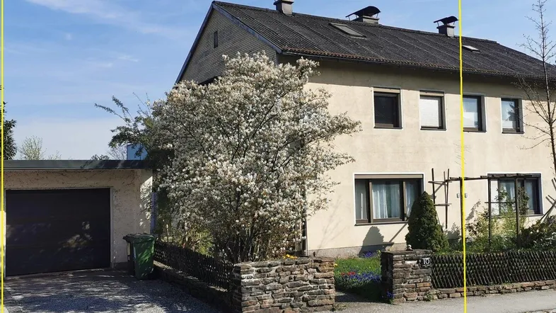 Einfamilienhaus mit Garage, Vorgarten und blühendem Baum an einem sonnigen Tag.