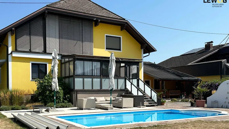 Gelbes Einfamilienhaus mit großem Garten, Pool und Sonnenterrasse unter blauem Himmel.