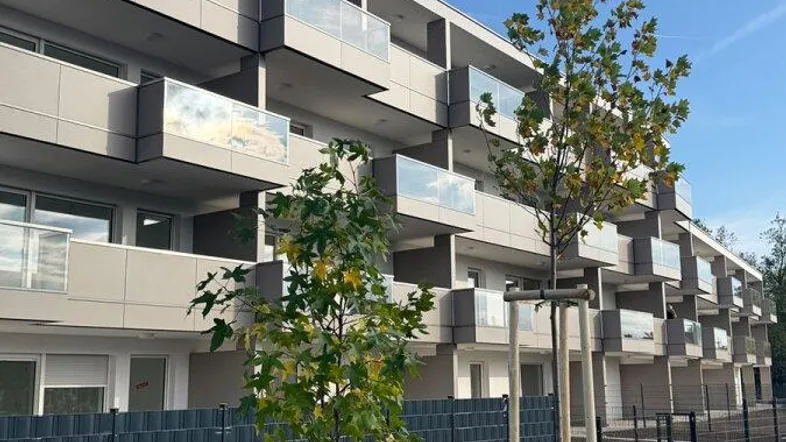 Modernes Mehrfamilienhaus mit Balkonen und neu angelegten Grünflächen unter blauem Himmel.