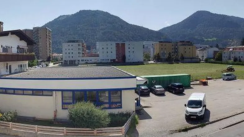 Panoramablick auf das Gebäude, den Parkplatz und die umliegende Landschaft mit Bergen im Hintergrund.