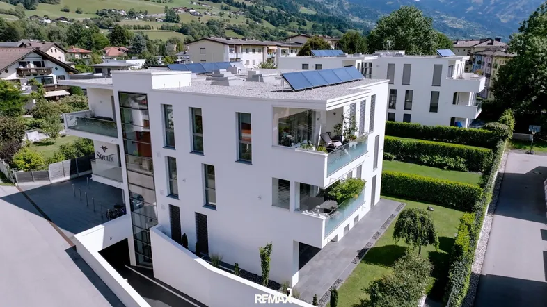 Moderne weiße Wohnanlage mit Balkonen, Solarpaneelen auf dem Dach und Bergblick.
