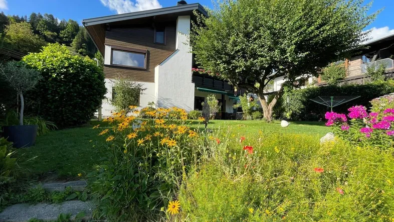 Gepflegter Garten mit blühenden Blumen und Blick auf das charmante Haus unter blauem Himmel.