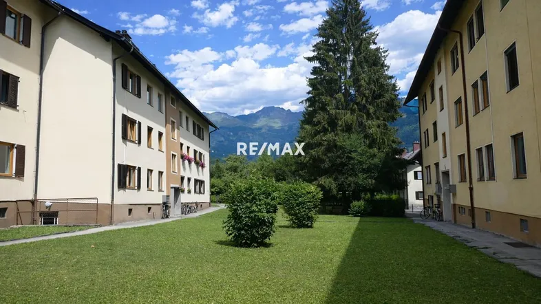 Mehrfamilienhäuser mit grüner Rasenfläche und Bergblick unter blauem Himmel.