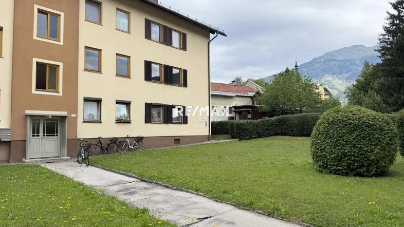 Mehrfamilienhaus mit gepflegter Rasenfläche und Blick auf die umliegenden Berge.