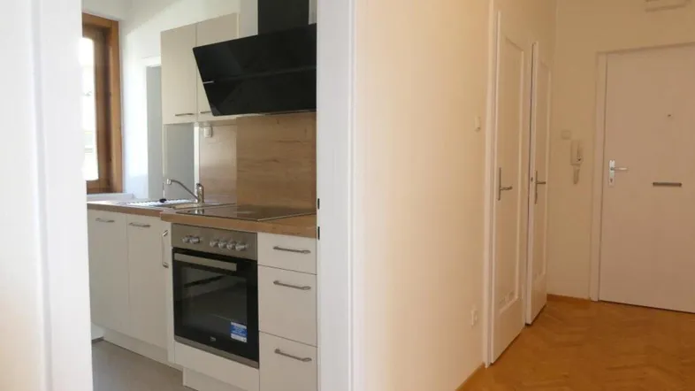 Moderne Einbauküche mit weißen Schränken, Kochfeld und Backofen, angrenzend an einen Flur mit Parkettboden.