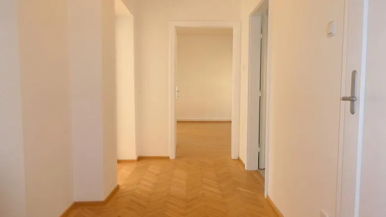 Heller Flur mit Fischgrätparkettboden und Zugang zu weiteren Räumen der Wohnung.