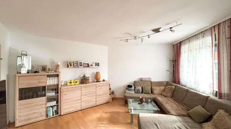 Gemütliches Wohnzimmer mit hellem Parkettboden, bequemer Eckcouch und modernen Holzschränken.