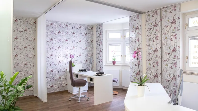 Heller und modern eingerichteter Geschäftsraum mit floraler Tapete, großem Fenster und Empfangsbereich.