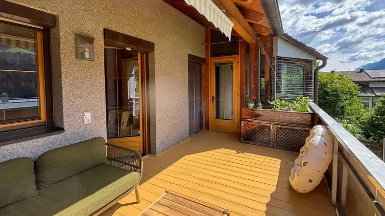 Geräumiger Balkon mit Holzboden, Sitzgelegenheiten und Markise, ideal zum Entspannen im Freien.