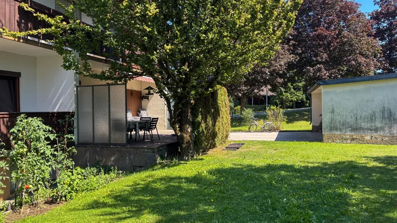 Überdachte Terrasse mit Gartenmöbeln und angrenzendem Rasenbereich, umgeben von Bäumen.