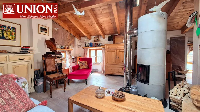 Gemütliches Wohnzimmer mit Holzbalkendecke, Kaminofen und rustikalen Möbeln unter dem Dach.