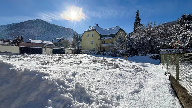 Gelbes Gebäude in verschneiter Landschaft mit Bergen im Hintergrund unter blauem Himmel und strahlender Sonne.