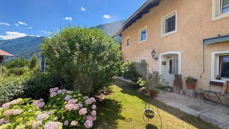 Charmantes Haus mit gepflegtem Garten, blühenden Hortensien und Bergblick unter blauem Himmel.