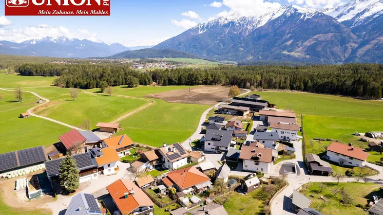 Luftaufnahme eines Dorfes mit Häusern, Feldern und majestätischen Bergen im Hintergrund.