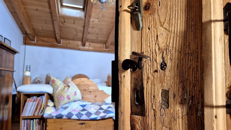 Rustikale Holztür öffnet sich zu einem gemütlichen Schlafzimmer mit Holzbalkendecke und Dachfenster.