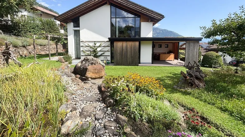Modernes Haus mit großen Fenstern, umgeben von einem gepflegten Garten und Bergblick.
