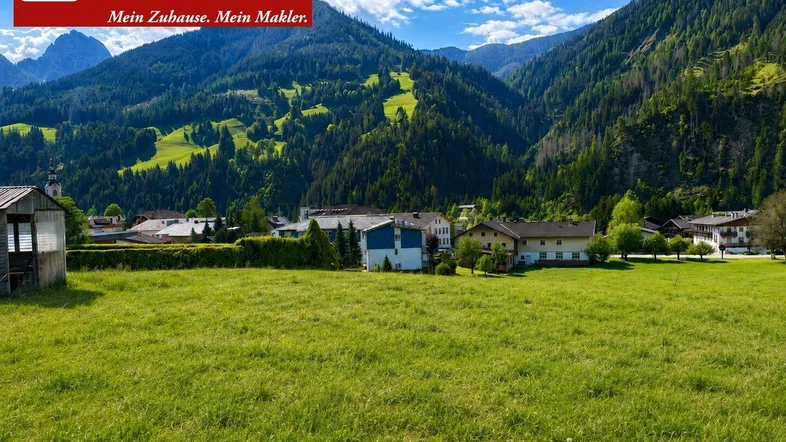 Weitläufige grüne Wiesen mit Blick auf ein malerisches Dorf und die umliegende Berglandschaft.
