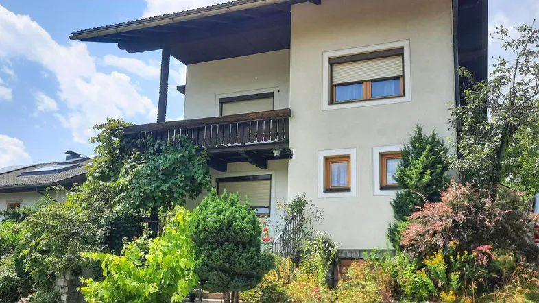 Ansicht des Hauses von außen mit Balkon, umgeben von üppigem Grün und Bäumen.