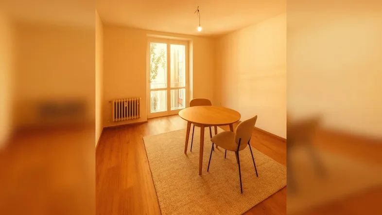 Helles Zimmer mit Holzboden, kleinem Esstisch und Zugang zu einem französischen Balkon.