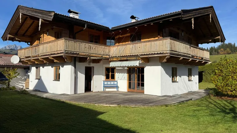 Traditionelles Holzhaus mit weißer Fassade, umlaufendem Balkon und großem Gartenbereich.
