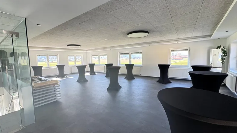 Großer, heller Raum mit mehreren Stehtischen, Akustikdecke und Fenstern mit Blick ins Grüne.