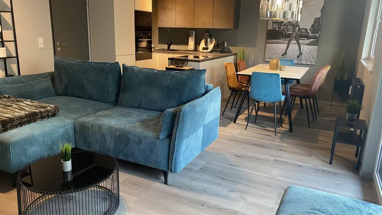 Moderner offener Wohn-Essbereich mit teal-farbenem Sofa, Esstisch und integrierter Küche.