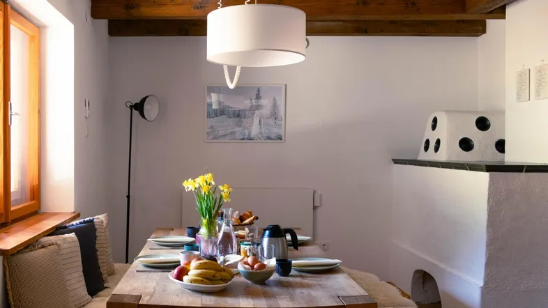 Gemütlicher Essbereich mit Holztisch, traditionellem Kachelofen und sichtbaren Deckenbalken.