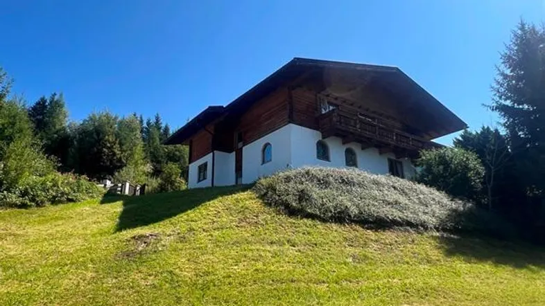 Traditionelles Chalet auf einem grünen Hügel mit Holzbalkonen und weitem Blick unter blauem Himmel.