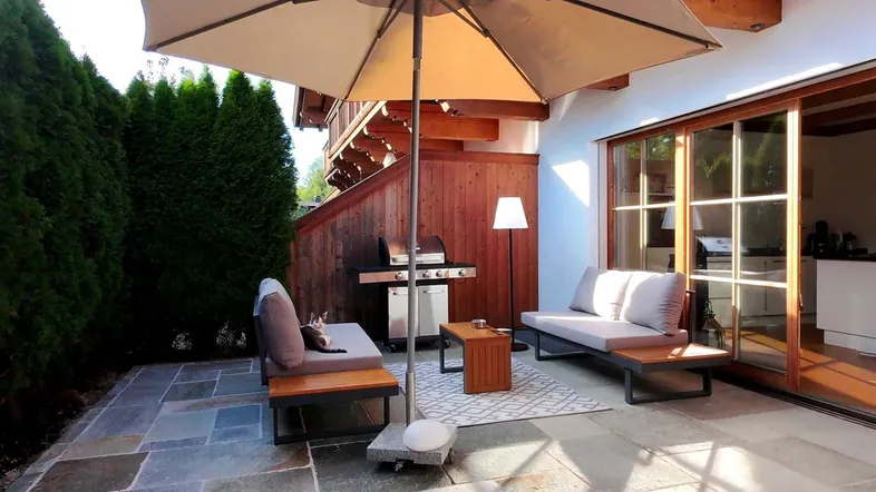 Geräumige Terrasse mit bequemen Sitzgelegenheiten, Sonnenschirm und Grillbereich, ideal für entspannte Stunden im Freien.