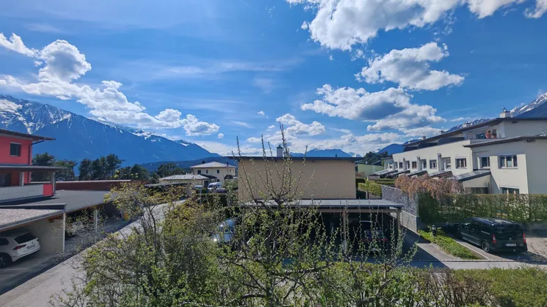 Panoramablick auf die umliegende Berglandschaft mit Wohnhäusern und Carports unter blauem Himmel.