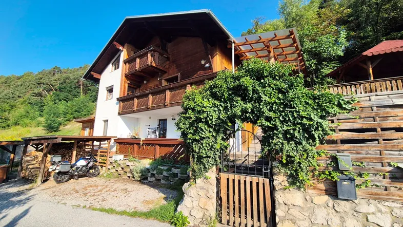 Ländliches Haus mit Holzfassade und Balkonen, umgeben von viel Grün und Bäumen.