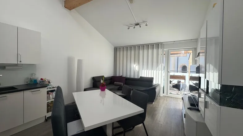 Heller offener Wohn-Essbereich mit integrierter Küche, Holzbalken und Zugang zum Balkon.