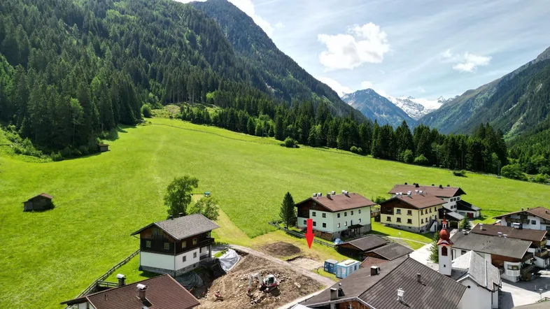 Luftaufnahme eines Dorfes in einem alpinen Tal, umgeben von grünen Wiesen und majestätischen Bergen.