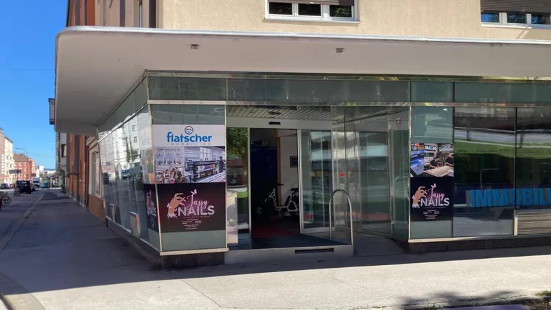 Die Außenansicht des Geschäftsgebäudes zeigt eine moderne Glasfassade mit Schaufenstern und einem Vordach.