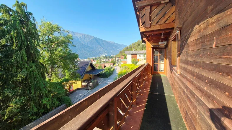 Sonniger Balkon mit Holzboden und Geländer, bietet einen weiten Blick auf das Tal und die Berge.
