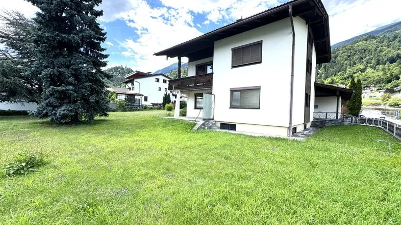 Großzügiger Gartenbereich mit Rasenfläche und Blick auf das Wohnhaus in alpiner Umgebung.