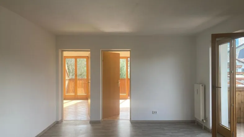 Helles, unmöbliertes Wohnzimmer mit Laminatboden und Zugang zu einem Balkon.