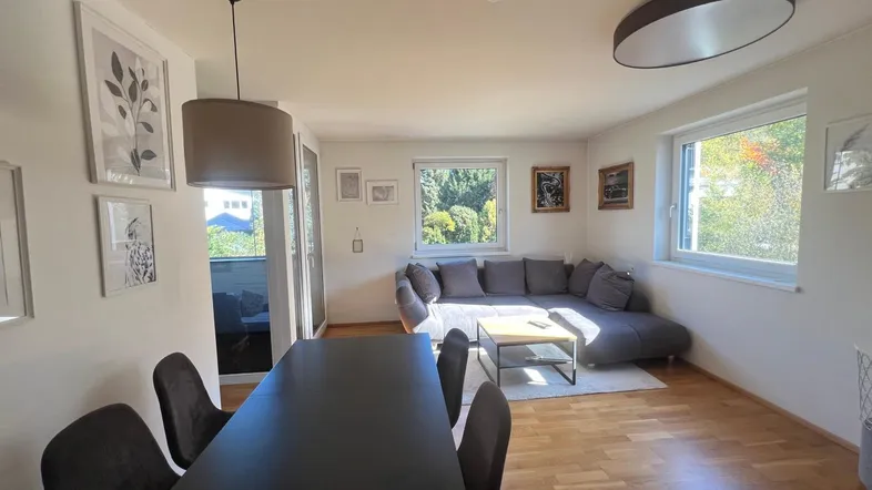 Heller Wohn- und Essbereich mit Holzboden, gemütlichem Sofa und Zugang zum Balkon.