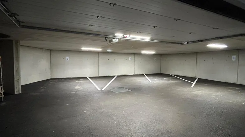 Geräumige Tiefgarage mit mehreren markierten Stellplätzen, Betonwänden und heller Deckenbeleuchtung.
