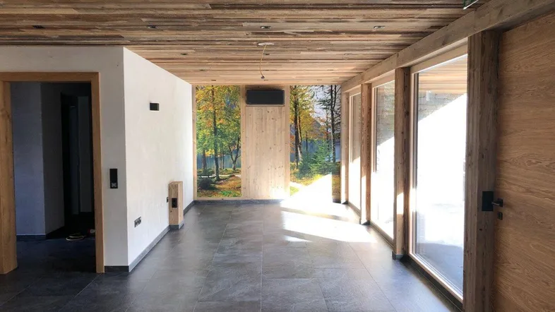 Geräumiger Innenraum mit dunklen Fliesen, Holzdecke und großen Fenstern, die viel Tageslicht hereinlassen.