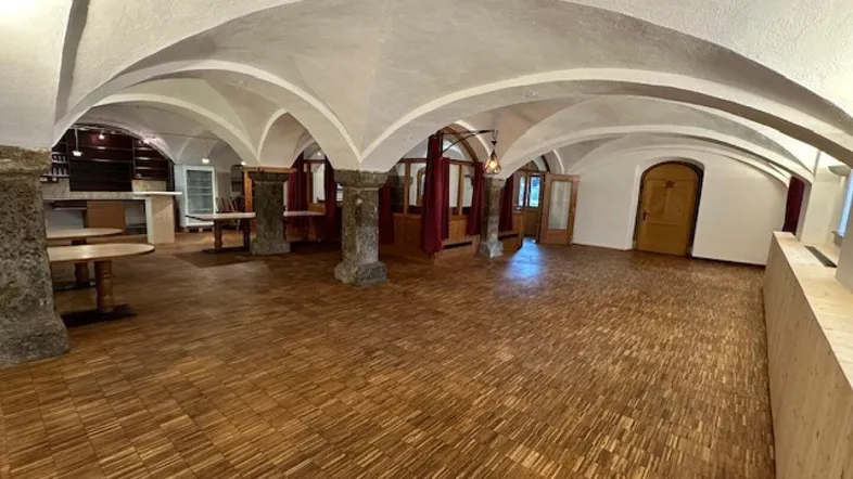 Geräumiger Gewerberaum mit Gewölbedecken, Holzboden und rustikalen Steinsäulen, ideal für Gastronomie.