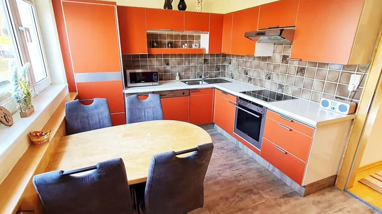 Moderne Küche mit orangefarbenen Fronten, integrierten Geräten und Essbereich am Fenster.
